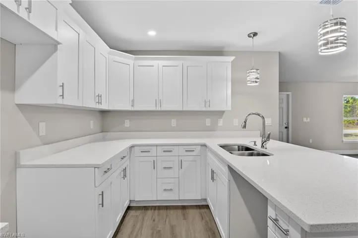 Kitchen featuring white cabinetry, a peninsula, light stone counters, and decorative light fixtures