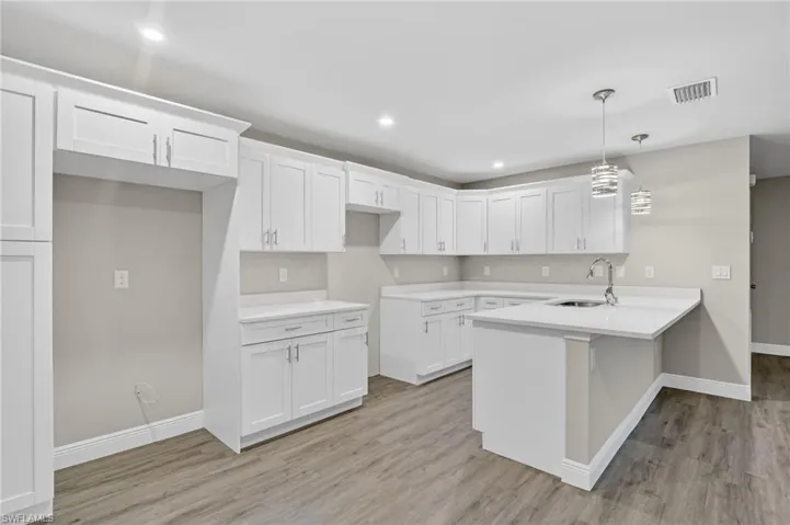 Kitchen featuring a peninsula, white cabinetry, pendant lighting, light wood-style flooring, and a breakfast bar area