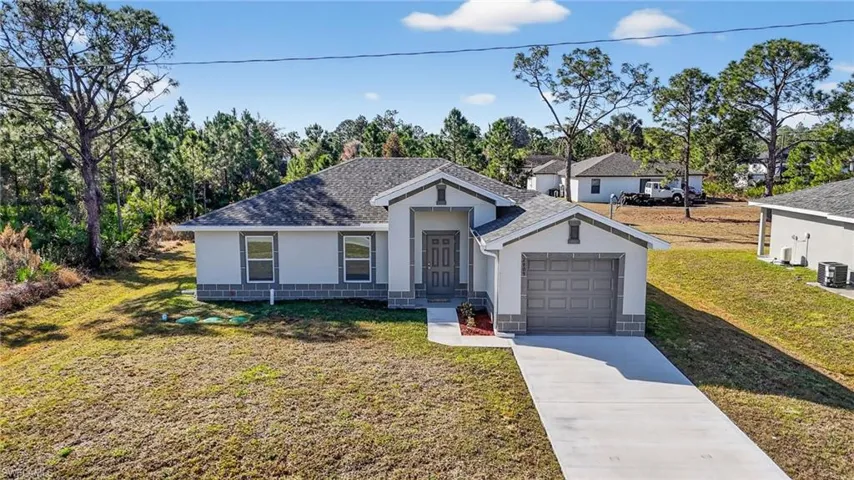 View of front facade featuring stucco siding, a front lawn, concrete driveway, a shingled roof, and a garage