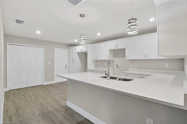 Kitchen with a peninsula, decorative light fixtures, light stone countertops, and white cabinets