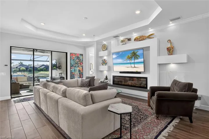 Living area featuring a raised ceiling, recessed lighting, a glass covered fireplace, crown molding, and wood finished floors