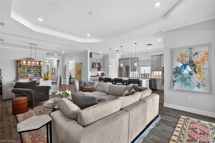 Living room featuring a raised ceiling, recessed lighting, dark wood-type flooring, and crown molding