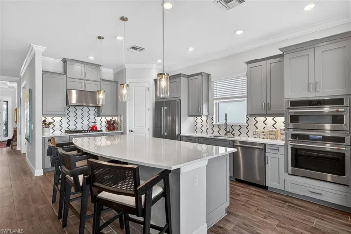 Kitchen featuring ornamental molding, gray cabinetry, a breakfast bar, hanging light fixtures, and decorative backsplash