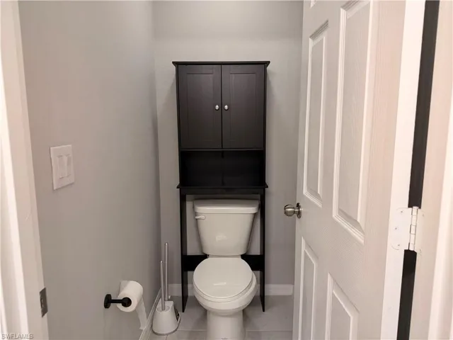 Bathroom featuring a white toilet with a black over-the-toilet storage cabinet, light gray walls, and light gray tile flooring