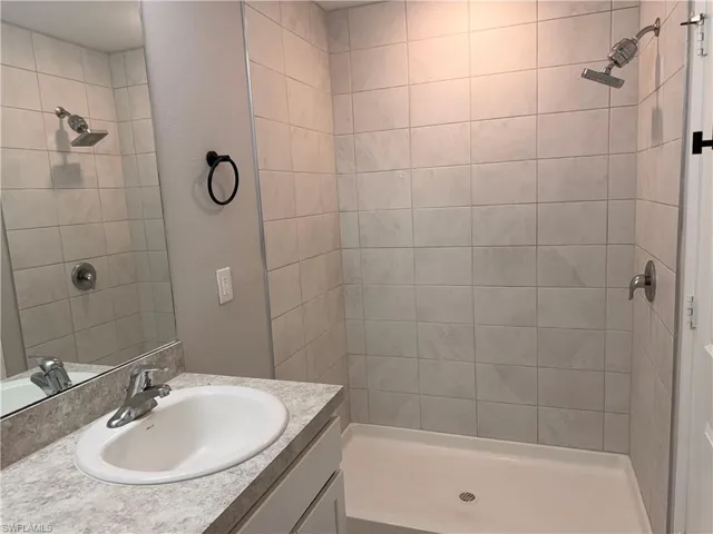 Bathroom featuring a walk-in shower with light-toned rectangular wall tiling, a rainfall showerhead, and a vanity with an integrated sink and laminate countertop