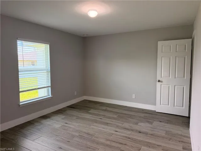 Neutral-toned room featuring wood-finish tile flooring, a multi-pane window with horizontal blinds, a ceiling-mounted light fixture, and a paneled interior door