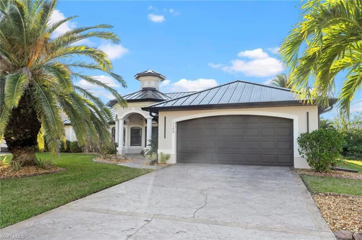 View of front of house with driveway, a front lawn, metal roof, and stucco siding