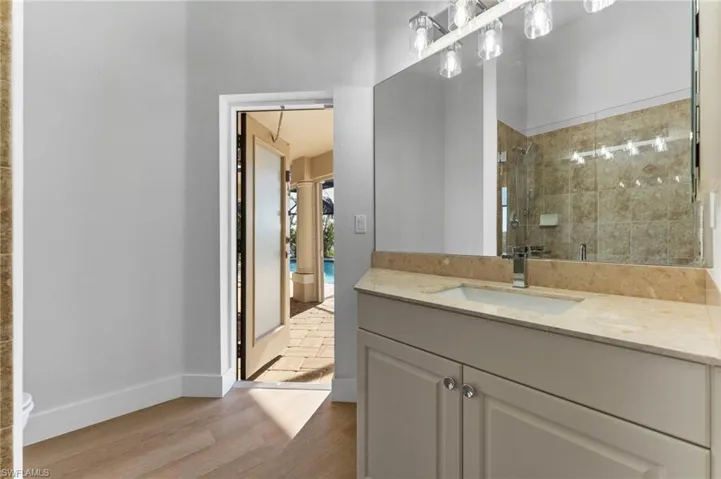 Full bath featuring a tile shower, vanity, baseboards, and wood finished floors