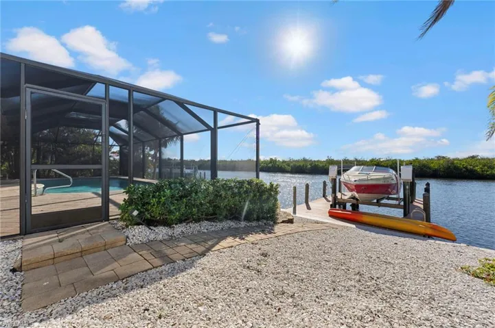 View of dock with a water view, glass enclosure, boat lift, and an outdoor pool