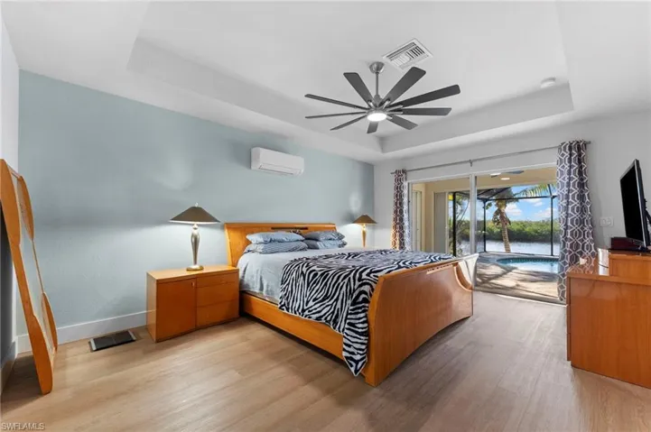 Bedroom featuring light wood finished floors, a wall unit AC, a raised ceiling, and visible vents
