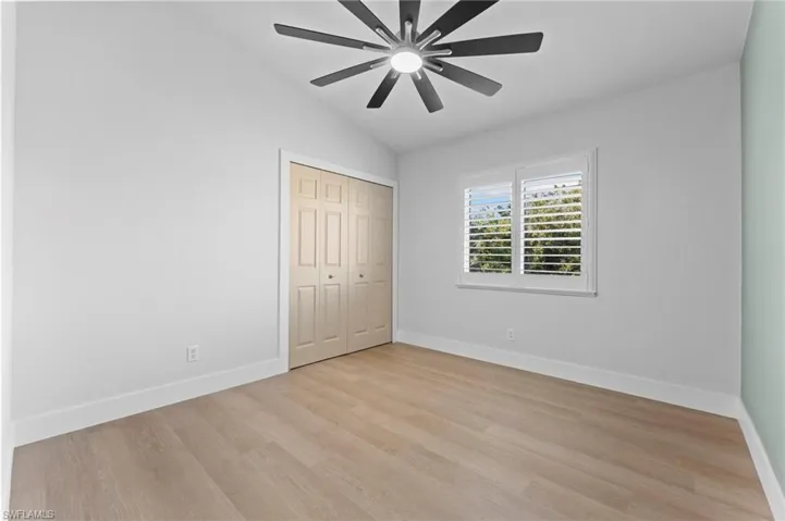 Unfurnished bedroom featuring ceiling fan, light wood-style flooring, baseboards, vaulted ceiling, and a closet