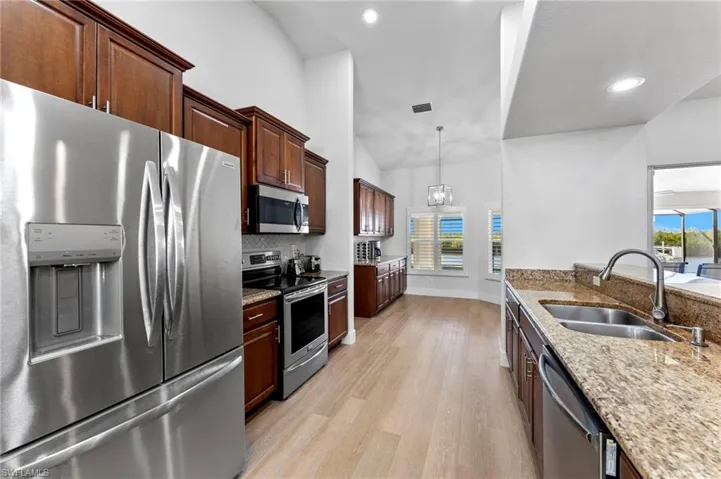 Kitchen featuring light stone counters, light wood-style flooring, a sink, vaulted ceiling, and appliances with stainless steel finishes