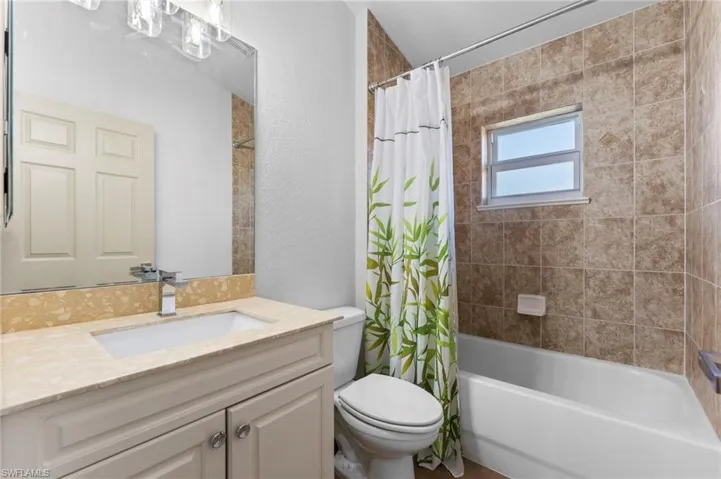Bathroom featuring a textured wall, vanity, toilet, and shower / bath combo with shower curtain