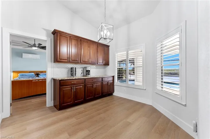 Kitchen with light stone counters, lofted ceiling, backsplash, a wall mounted AC, and light wood-type flooring