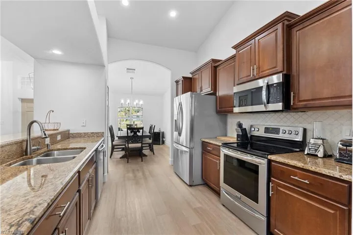 Kitchen with appliances with stainless steel finishes, light wood-type flooring, a sink, and light stone countertops