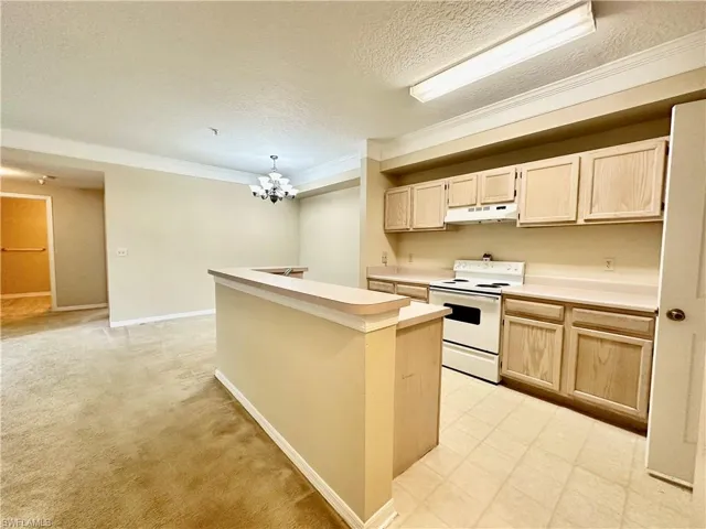 Kitchen with light brown cabinetry, a notable chandelier, crown molding, light colored carpet, and white electric stove