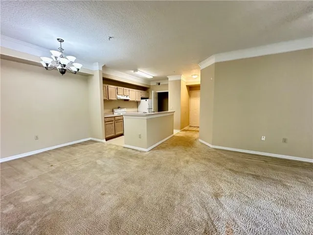 Unfurnished living room with light carpet, a notable chandelier, a textured ceiling, and crown molding