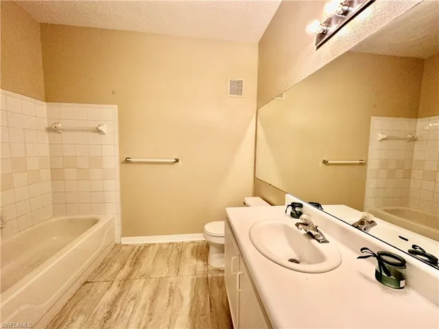 Full bathroom featuring a textured ceiling, toilet, vanity, and tiled shower / bath