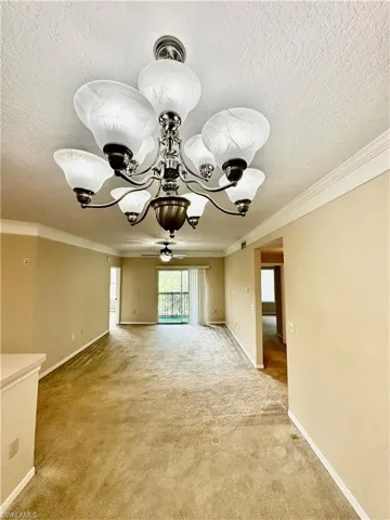 Empty room featuring a textured ceiling, carpet, an inviting chandelier, and crown molding