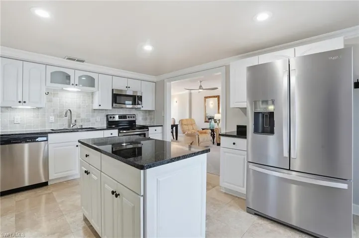 Kitchen with stainless steel appliances, dark stone counters, white cabinets, a ceiling fan, and backsplash
