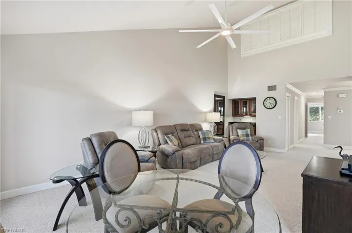 Living area featuring a towering ceiling, light colored carpet, a ceiling fan, and ornamental molding