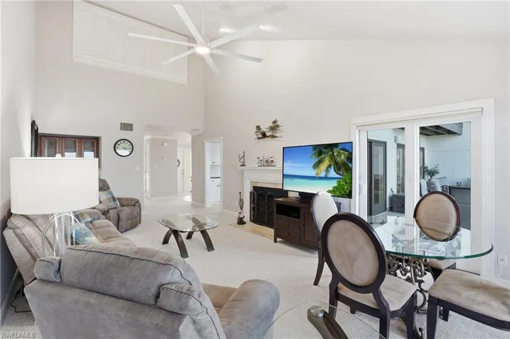 Carpeted living area featuring a fireplace with flush hearth, a high ceiling, and ceiling fan