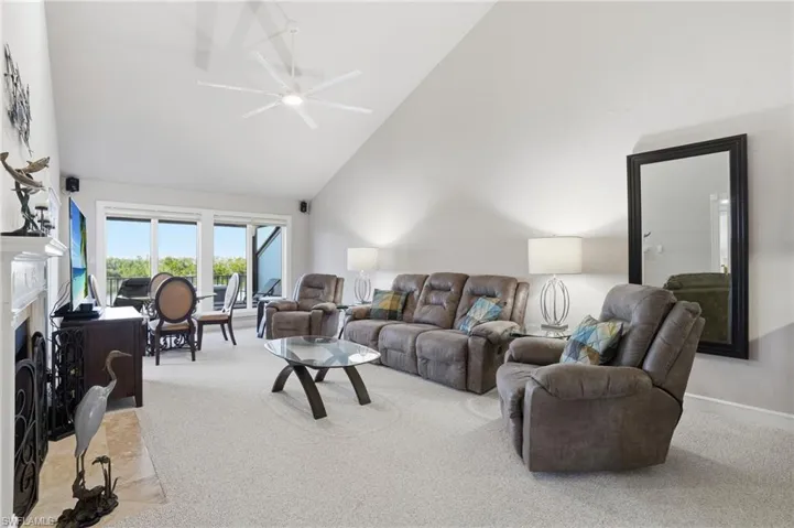 Carpeted living area with high vaulted ceiling, a fireplace, and ceiling fan