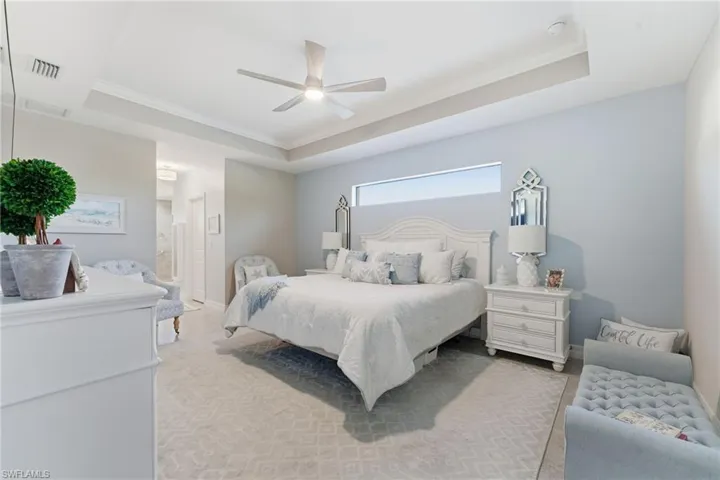 Bedroom featuring a tray ceiling, ceiling fan, ornamental molding, and connected bathroom