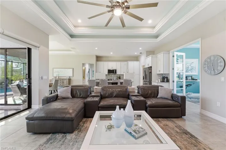 Living area with crown molding, a ceiling fan, a raised ceiling, recessed lighting, and light tile patterned floors