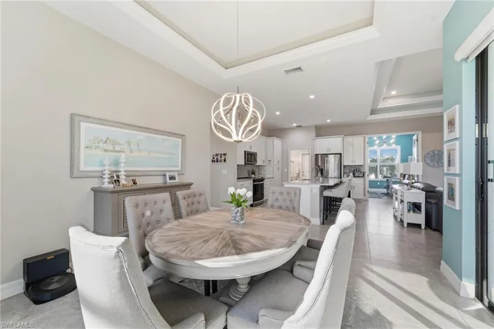 Dining area with a raised ceiling, a chandelier, ornamental molding, and recessed lighting