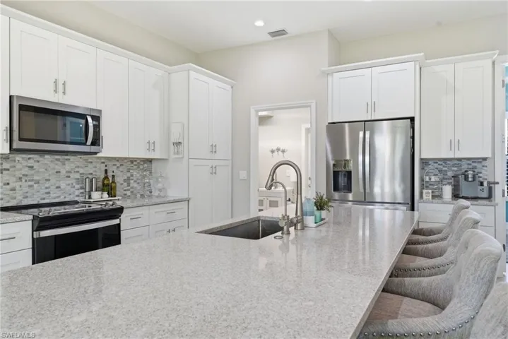 Kitchen featuring decorative backsplash, appliances with stainless steel finishes, white cabinetry, light stone countertops, and a kitchen breakfast bar