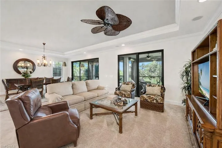 Living room featuring a raised ceiling, ornamental molding, a chandelier, and a ceiling fan