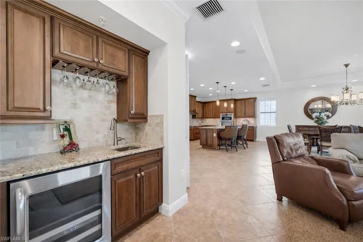 Kitchen with beverage cooler, a kitchen breakfast bar, wood finish cabinets, tasteful backsplash, and hanging lights