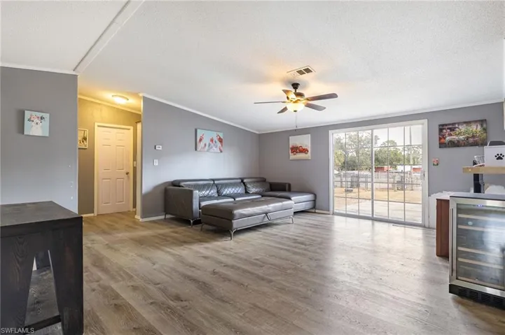 Living area featuring wine cooler, crown molding, light wood finished floors, a ceiling fan, and a textured ceiling
