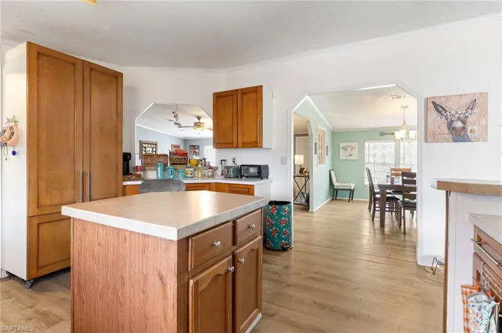 Kitchen with arched walkways, a kitchen island, ornamental molding, wood finish cabinetry, and light countertops