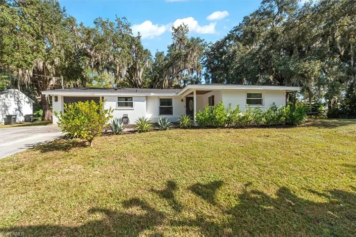 Ranch-style home with stucco siding, a front lawn, view of scattered trees, and concrete driveway