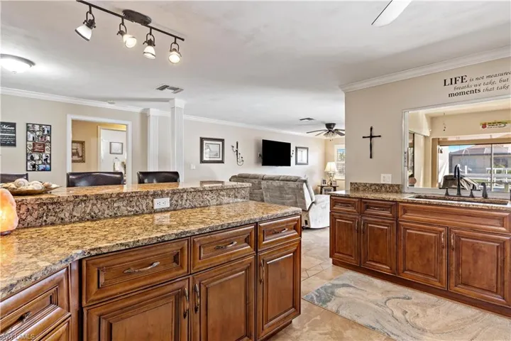 Kitchen featuring ornate columns, sink, light stone countertops, crown molding, and ceiling fan