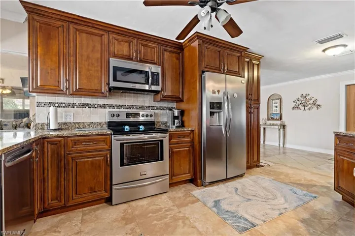Kitchen with decorative backsplash, stainless steel appliances, ornamental molding, light stone countertops, and ceiling fan