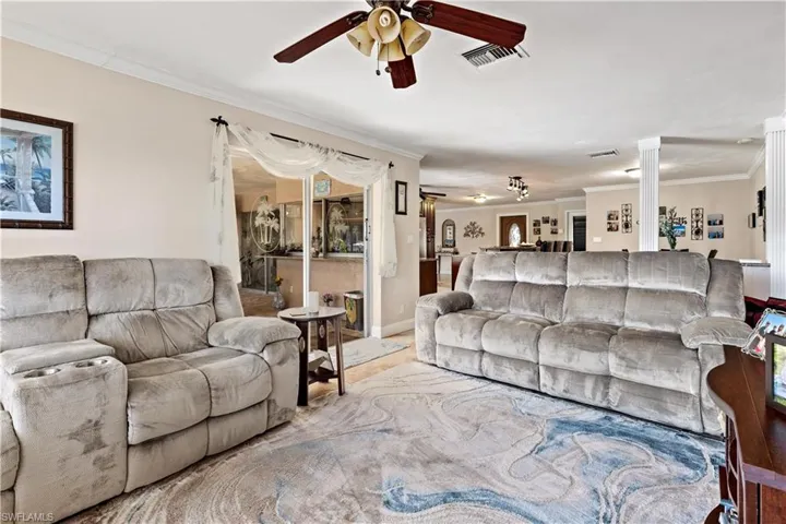 Living room with ornamental molding, ornate columns, and ceiling fan