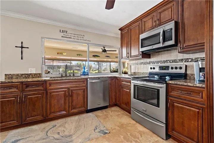 Kitchen with light stone countertops, sink, light tile patterned flooring, stainless steel appliances, and crown molding