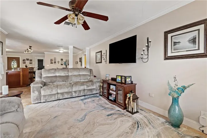 Living room with decorative columns, crown molding, and ceiling fan