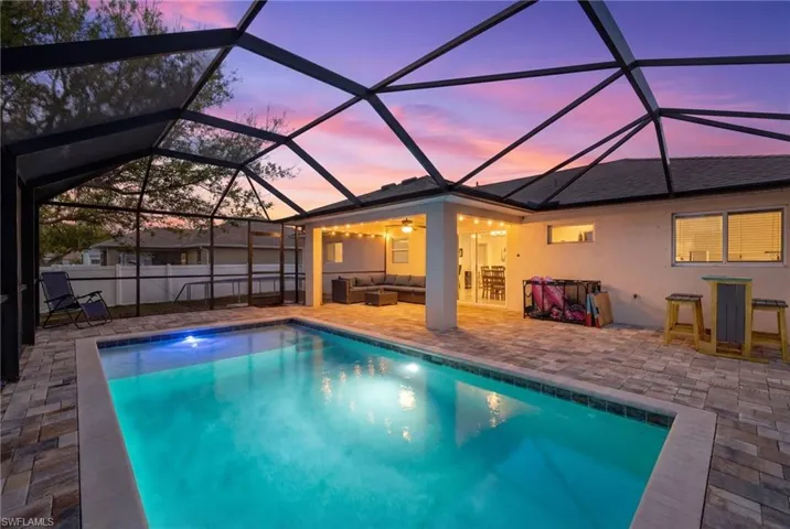 Pool at dusk featuring a sunroom, glass enclosure, an outdoor hangout area, and a patio