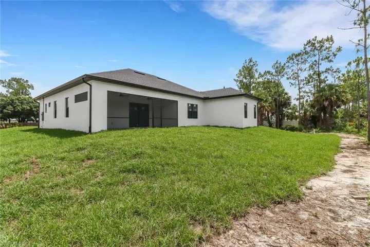 Back of property featuring a screened lanai and landscaped area