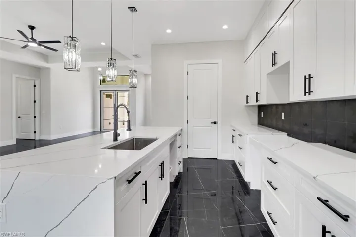 Kitchen featuring a center island with sink, backsplash, white cabinets, modern pendant and recessed lighting