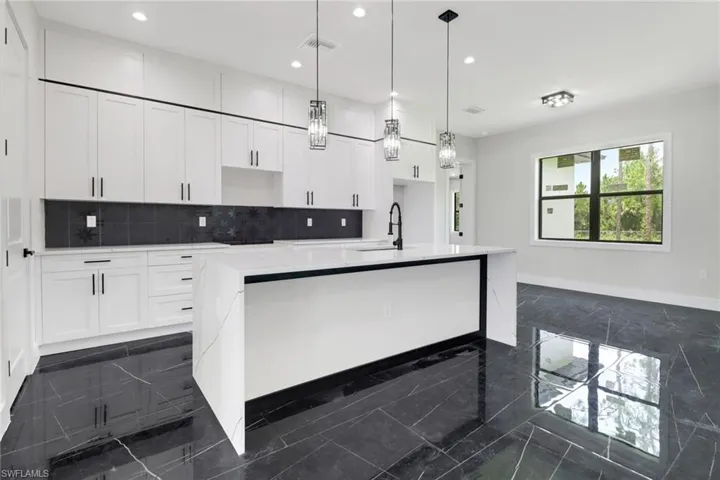 Kitchen with a waterfall island with sink, white cabinets, tasteful backsplash, pendant and recessed lighting, and tile flooring