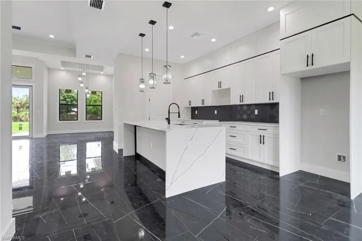 Kitchen featuring tile floors, backsplash, a kitchen waterfall island with sink, white cabinetry, and light quartz counters