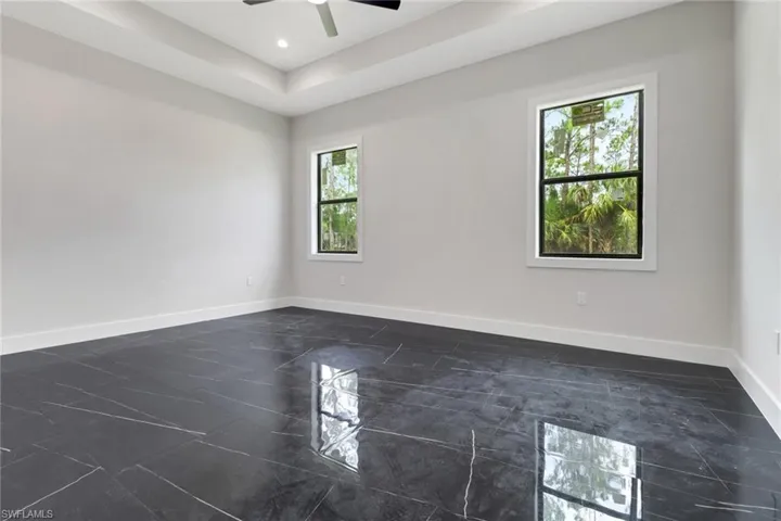 Primary bedroom with tile floors, tray ceiling, recessed lighting and ceiling fan