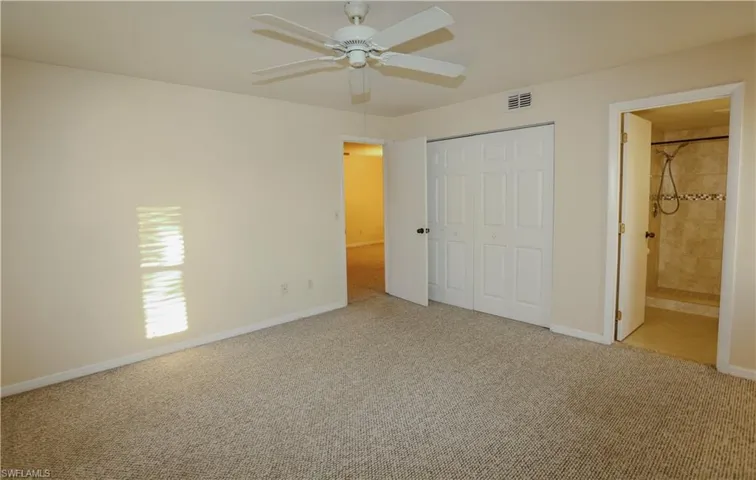 Unfurnished bedroom with light carpet, a closet, connected bathroom, and a ceiling fan