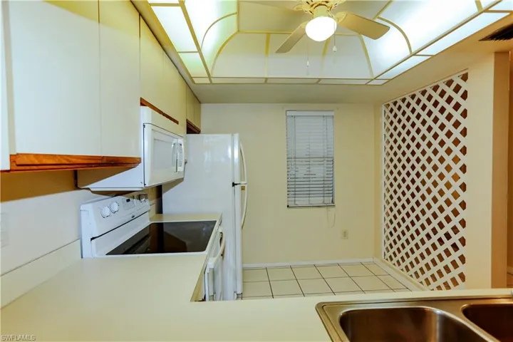 Kitchen with light countertops, white appliances, light tile patterned flooring, brown cabinets, and a ceiling fan
