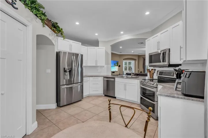 Kitchen featuring light tile patterned flooring, ornamental molding, backsplash, white cabinetry, and appliances with stainless steel finishes